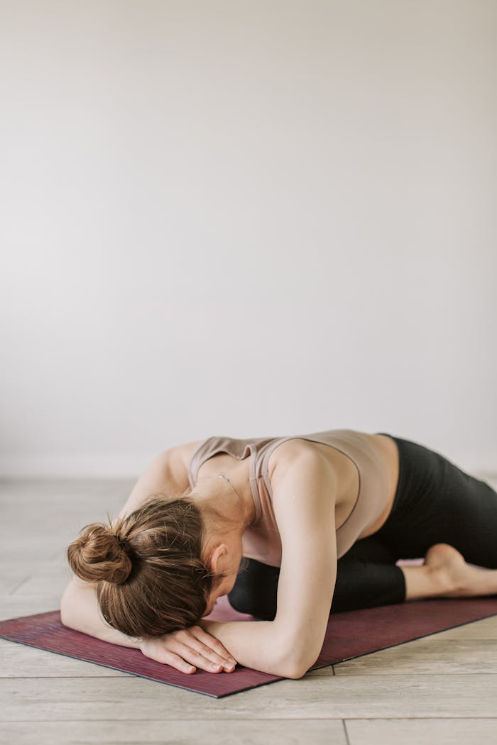 A woman practicing child's pose on a yoga mat indoors for relaxation and mindfulness.