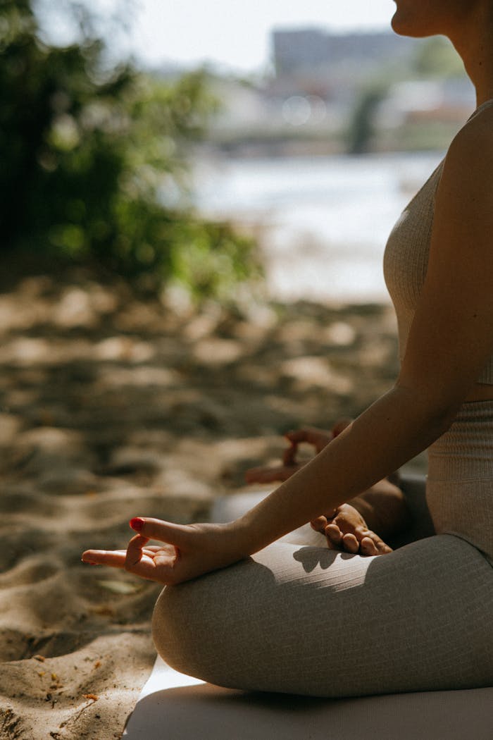 A woman practices yoga and meditation on a sandy beach, bathed in soft natural light.